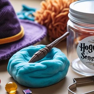 May include: A sensory kit with a purple witch hat, blue playdough with a wand, and a jar labeled "Hogwarts Sensory Kit." The kit includes colorful gems and a cookie cutter. Orange and yellow pom-poms are also visible.