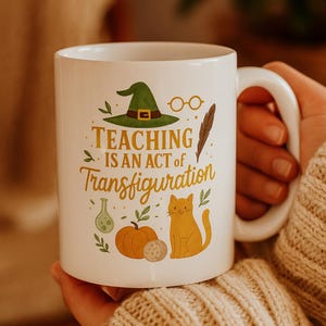 May include: White ceramic mug with the text "TEACHING IS AN ACT OF Transfiguration" in gold lettering. The mug features illustrations of a witch hat, glasses, a feather, a pumpkin, a cat, and other magical elements.