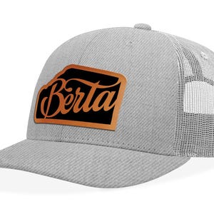 May include: A grey and white trucker hat with a brown leather patch that says "Berta" in black lettering.