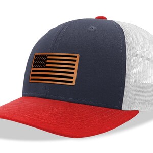 May include: A navy blue and red trucker hat with a brown leather American flag patch on the front.