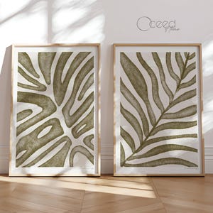 May include: Two framed prints with abstract green leaf designs. The prints are on a white background and have a subtle texture. The frames are a light wood color.