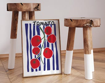 Op de afbeelding: Twee houten krukken met natuurlijke houten bladen en wit geschilderde poten flankeren een ingelijste print. De print toont een tomatenillustratie met het woord "TOMATO" erboven. De achtergrond van de print heeft blauwe verticale strepen.