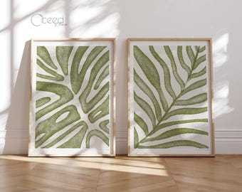 May include: Two framed prints of green botanical illustrations. The print on the left features a stylized monstera leaf. The print on the right features a stylized palm leaf.