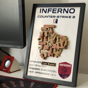 Könnte beinhalten: Gerahmtes Kunstwerk mit der Inferno-Karte aus Counter-Strike 2. Die 3D-Reliefkarte ist in Braun- und Beigetönen gehalten. Der Text enthält "INFERNO" und "COUNTER-STRIKE 2". Zusätzlicher Text gibt den Operator, den Ort, das Szenario und das erste Erscheinen an.