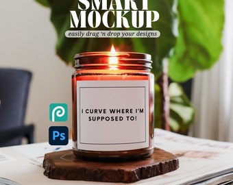 May include: A brown glass candle jar with a white label that reads "I curve where I'm supposed to!" The candle is lit and sitting on a wooden coaster on top of a stack of magazines.