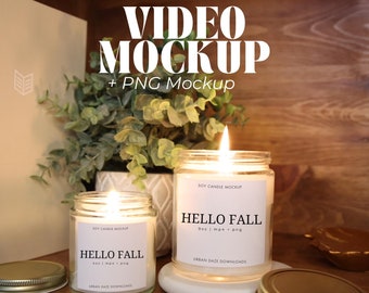 May include: Two soy candles with white labels that say "Soy Candle Mockup" and "Hello Fall" with the size of the candle in ounces and the file type. The candles are lit and sitting on a wooden shelf with a green plant in the background.