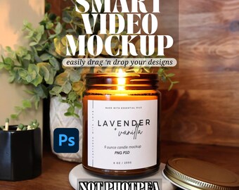 May include: A brown glass candle jar with a white label that reads "LAVENDER + vanilla" and "9 ounce candle mockup PNG PSD 9 OZ / 255G". The candle is lit and the jar is sitting on a wooden surface. The text "SMART VIDEO MOCKUP easily drag 'n drop your designs" is at the top of the image. The text "NOT PHOTPEA COMPATIBLE" is at the bottom of the image.