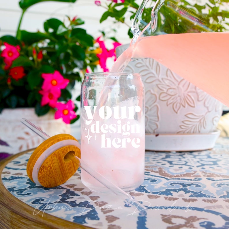 May include: A clear glass can with a bamboo lid and a straw, filled with a pink beverage. The can has the text "your design here" printed on it. The can is being poured into from a glass pitcher.
