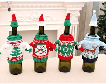 Può includere: Quattro bottiglie di vino vestite con maglioni natalizi festosi con cappelli di Babbo Natale. I maglioni presentano un pupazzo di neve, un albero di Natale, una renna e la parola "GIOIA".