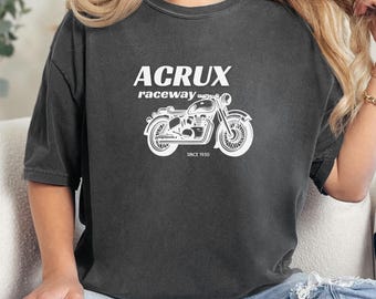 May include: Dark gray t-shirt with a white graphic of a vintage motorcycle and the text "ACRUX raceway SINCE 1950". The shirt is worn by a person sitting on a cream-colored couch.