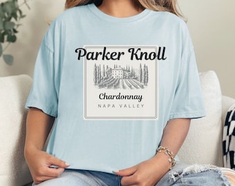Puede incluir: Una camiseta azul claro con un gráfico de una etiqueta de botella de vino que dice "Parker Knoll Chardonnay Napa Valley".