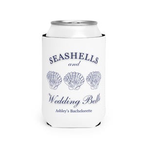 Może przedstawiać: Biała osłona na puszkę z granatowym tekstem i ilustracjami muszli. Tekst brzmi "SEASHELLS and Wedding Bells" z "Ashley's Bachelorette" poniżej. Zaprojektowany, aby napoje były zimne.