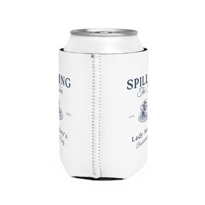 May include: White can cooler with a blue and white design. The text on the cooler reads "Spilling The Tea est. Lady As... Bottled and Brewed".