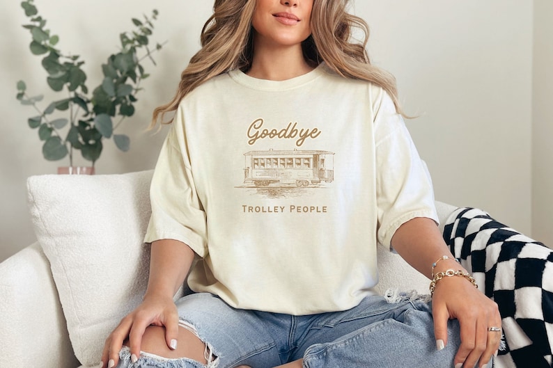 May include: A cream-coloured t-shirt with a brown graphic of a trolley and the text "Goodbye Trolley People".