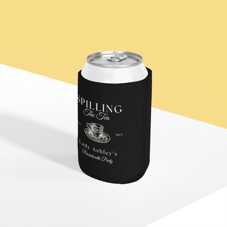 May include: Black can cooler with white text that reads "Spilling the Tea" with a small teacup graphic and "Lady Ashley's Bachelorette Party".