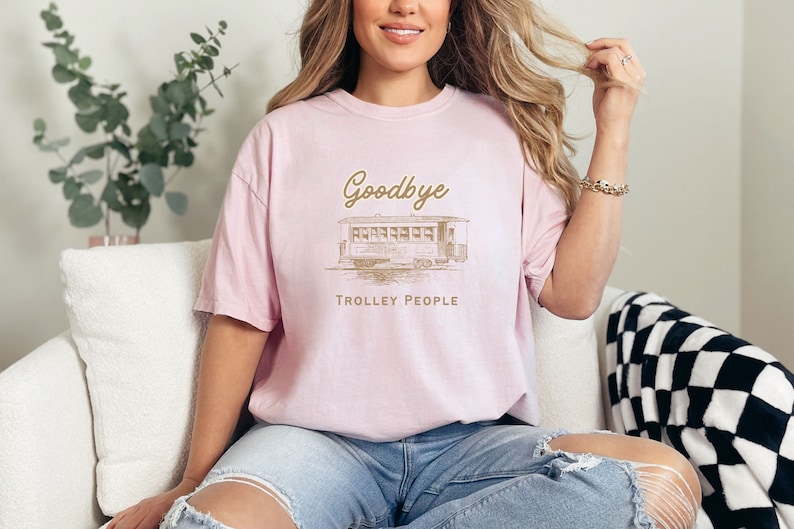 May include: A pink t-shirt featuring a vintage-style illustration of a tram and the text "Goodbye Trolley People".