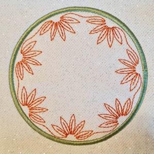 May include: A round embroidery design with a green outer ring and an orange floral pattern around the edge.