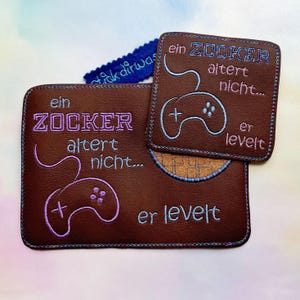 May include: Two brown leather coasters with embroidered text and a game controller design. The text reads "ein ZOCKER altert nicht... er levelt".