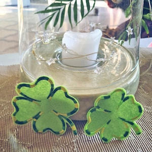 May include: A glass cloche with a white candle and fairy lights inside. Two green shamrock-shaped decorations are on a beige surface.