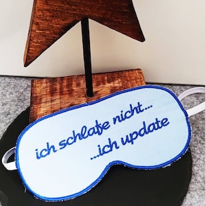 May include: A light blue sleep mask with a blue embroidered message that reads "ich schlafe nicht... ich update".