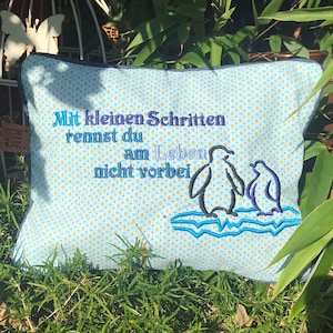 May include: A blue and white pillow with a penguin design and the text "Mit kleinen Schritten rennst du am Leben nicht vorbei".