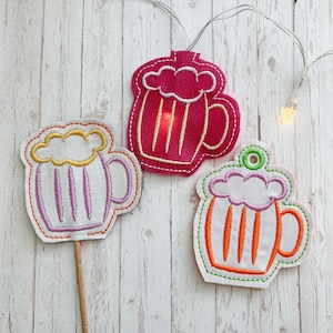 May include: Three felt beer mug ornaments with embroidered details. The mugs are in pink, orange, and white with yellow foam.