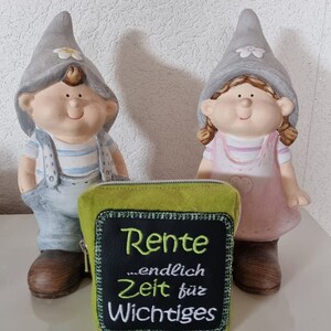 Puede incluir: Una bolsa de fieltro verde con cierre de cremallera y un parche de fieltro negro que dice "Rente ...endlich Zeit f&uuml;r Wichtiges". Dos peque&ntilde;os gnomos grises con caras pintadas est&aacute;n detr&aacute;s de la bolsa.