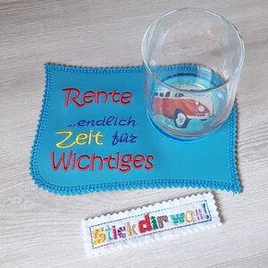Puede incluir: Un posavasos azul con el texto "Rente ...endlich Zeit f&uuml;r Wichtiges" bordado en &eacute;l. Un vaso con una imagen de una furgoneta Volkswagen roja est&aacute; encima del posavasos. Un peque&ntilde;o parche blanco con el texto "stick dir was!" est&aacute; en la mesa.