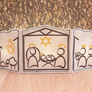 May include: A three-panel embroidered Christmas nativity scene with a brown wooden frame. The center panel depicts the Holy Family with a star above them. The left panel shows a shepherd with a sheep and an angel. The right panel shows three wise men with gifts.