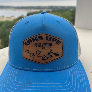 Könnte beinhalten: Eine blaue und graue Trucker-Kappe mit einem Holz-Patch, auf dem "Lake Life Point Venture TX" steht und ein Seeumriss abgebildet ist.