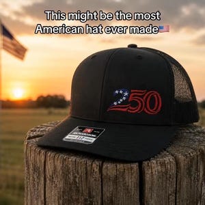 May include: Black trucker hat with a mesh back, featuring an embroidered design of the number "250" in red, white, and blue. The hat is displayed on a wooden post with an American flag waving in the background. Text on the hat reads "This might be the most American hat ever made."