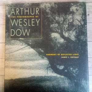 May include: A book titled "Arthur: The Photographs of Wesley Dow" with a dark cover featuring a tree silhouette and the text "Harmony of Reflected Light". The book has a vintage aesthetic.