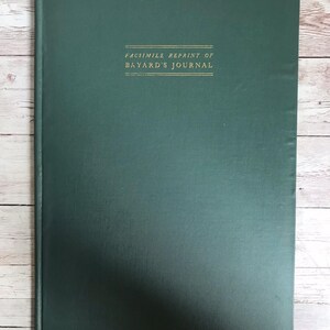 May include: A dark green book with the title "FACSIMILE REPRINT OF BAYARD'S JOURNAL" in gold lettering. The book has a textured cover with vertical lines. The book is rectangular and appears to be a journal or notebook.