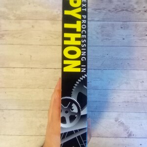 May include: A black book spine with the title "PYTHON" in large yellow letters. The book is titled "TEXT PROCESSING IN" and has the author's name "MERTZ" at the top. The publisher's logo is at the bottom.