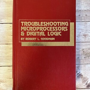 May include: A red hardcover book with the title "Troubleshooting Microprocessors & Digital Logic" in gold lettering on the front cover. The author's name, "By Robert L. Goodman", is also printed in gold lettering below the title.