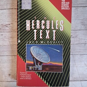 May include: A paperback book titled "The Hercules Text" by Jack McDevitt. The cover features a graphic of a radio telescope under a starry sky. The book has a red, black, and yellow design with the text "The New Ace Science Fiction Specials".