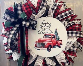 May include: A Christmas wreath with a circular centerpiece featuring a red vintage truck carrying a Christmas tree. The wreath is made of red, black, and white plaid ribbons, with green accents and the text "have yourself a merry little Christmas".