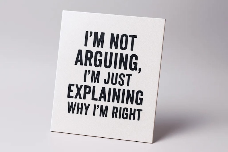 Op de afbeelding: Een wit rechthoekig bord met zwarte tekst: "I'M NOT ARGUING, I'M JUST EXPLAINING WHY I'M RIGHT." Het bord staat schuin tegen een effen witte achtergrond.