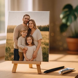 Op de afbeelding: Een familieportret op een kleine ezel. Het canvas toont een lachende familie van vier. De ezel is gemaakt van lichtgekleurd hout en de sc&egrave;ne speelt zich af op een houten oppervlak met een pen en een tube verf.