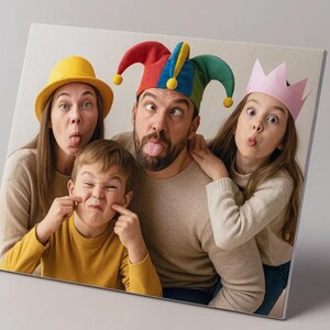 Op de afbeelding: Een canvas print met een gezin van vier dat gekke gezichten trekt. De volwassenen dragen een gele hoed en een narrenmuts, terwijl de kinderen een geel shirt en een roze kroon dragen. De afbeelding is schuin.