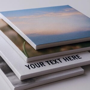 Op de afbeelding: Een stapel vierkante canvas prints met verschillende afbeeldingen. De bovenste print toont een blauwe lucht met wolken. De tweede print toont een landschap. De derde print heeft de tekst "YOUR TEXT HERE". De onderste print is een zwart-wit afbeelding.