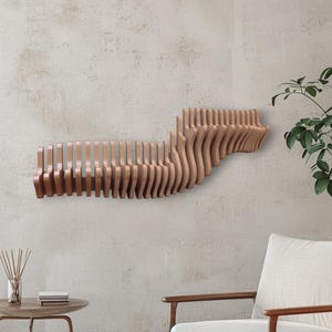 Op de afbeelding: Een modern wandrek van lichtbruin hout. Het rek heeft een uniek, golvend ontwerp, met verticale lamellen die een gelaagd effect creëren. Het rek is ongeveer 122 cm lang en is bevestigd aan een neutraal gekleurde muur.
