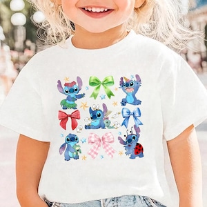 A young girl with blonde hair is smiling and wearing a white t-shirt with a graphic of Stitch and other characters from the Disney movie.