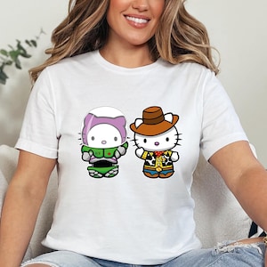 A woman wearing a white t-shirt with two cartoon characters, one wearing a green outfit and the other a cowboy hat, sitting on a couch.