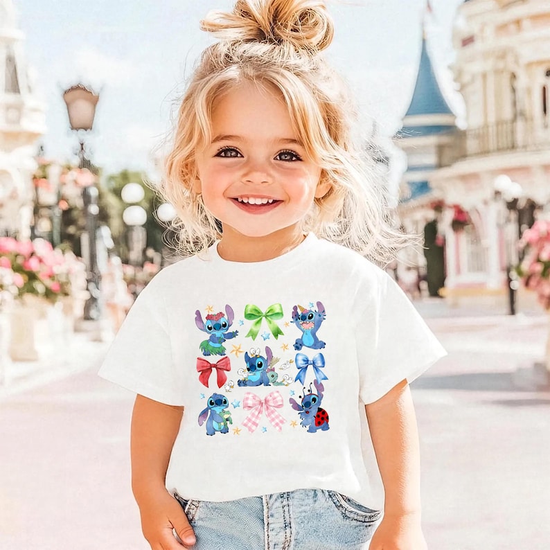 A young girl with blonde hair is smiling and wearing a white t-shirt with a graphic of Stitch and other characters from the Disney movie.