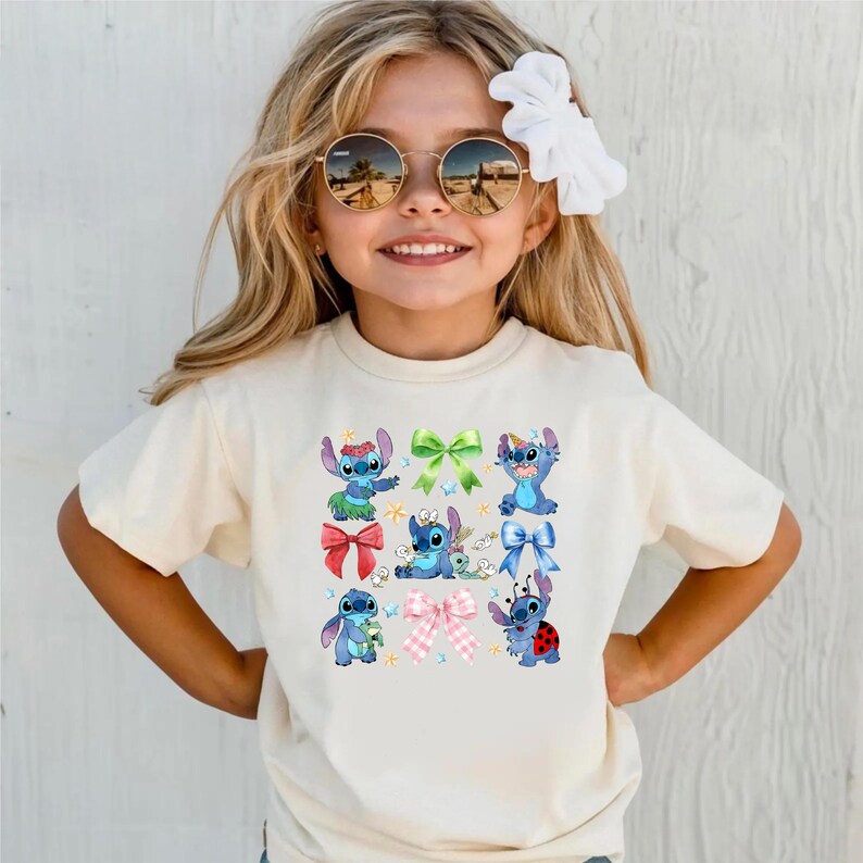 A young girl wearing a white t-shirt with a graphic of various cartoon characters, including Stitch, and a bow in her hair.