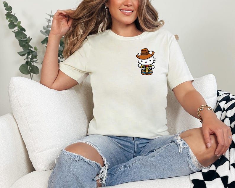 A woman sitting on a couch wearing a white t-shirt with a Hello Kitty graphic and distressed jeans.