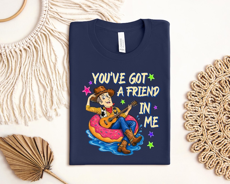 A blue t-shirt with a cartoon image of a man playing a guitar while sitting on a donut, surrounded by stars and text that says "You've Got a Friend in Me".