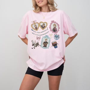 A woman wearing a pink t-shirt with various cartoon characters and text printed on it.