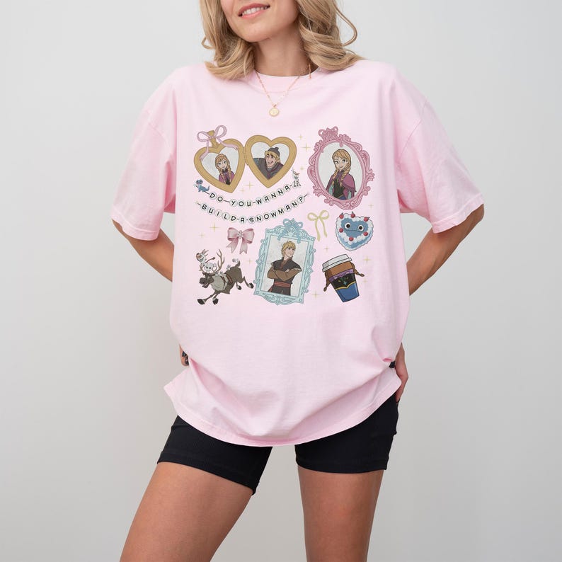 A woman wearing a pink t-shirt with various cartoon characters and text printed on it.